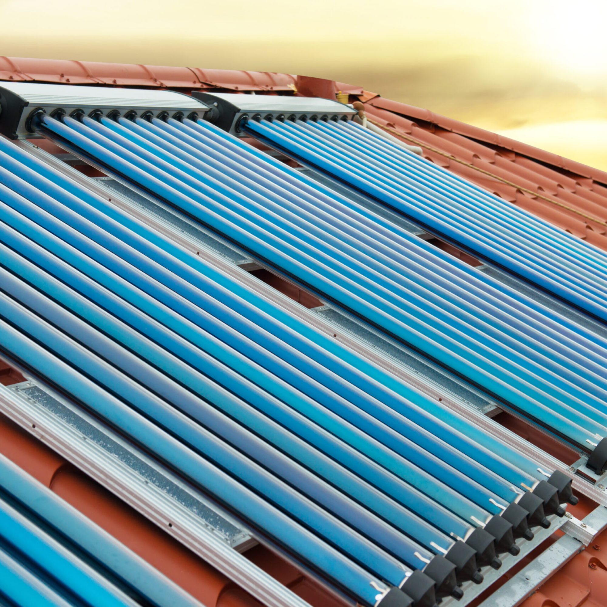 Vacuum collectors- solar water heating system on red roof of the house under shining sun