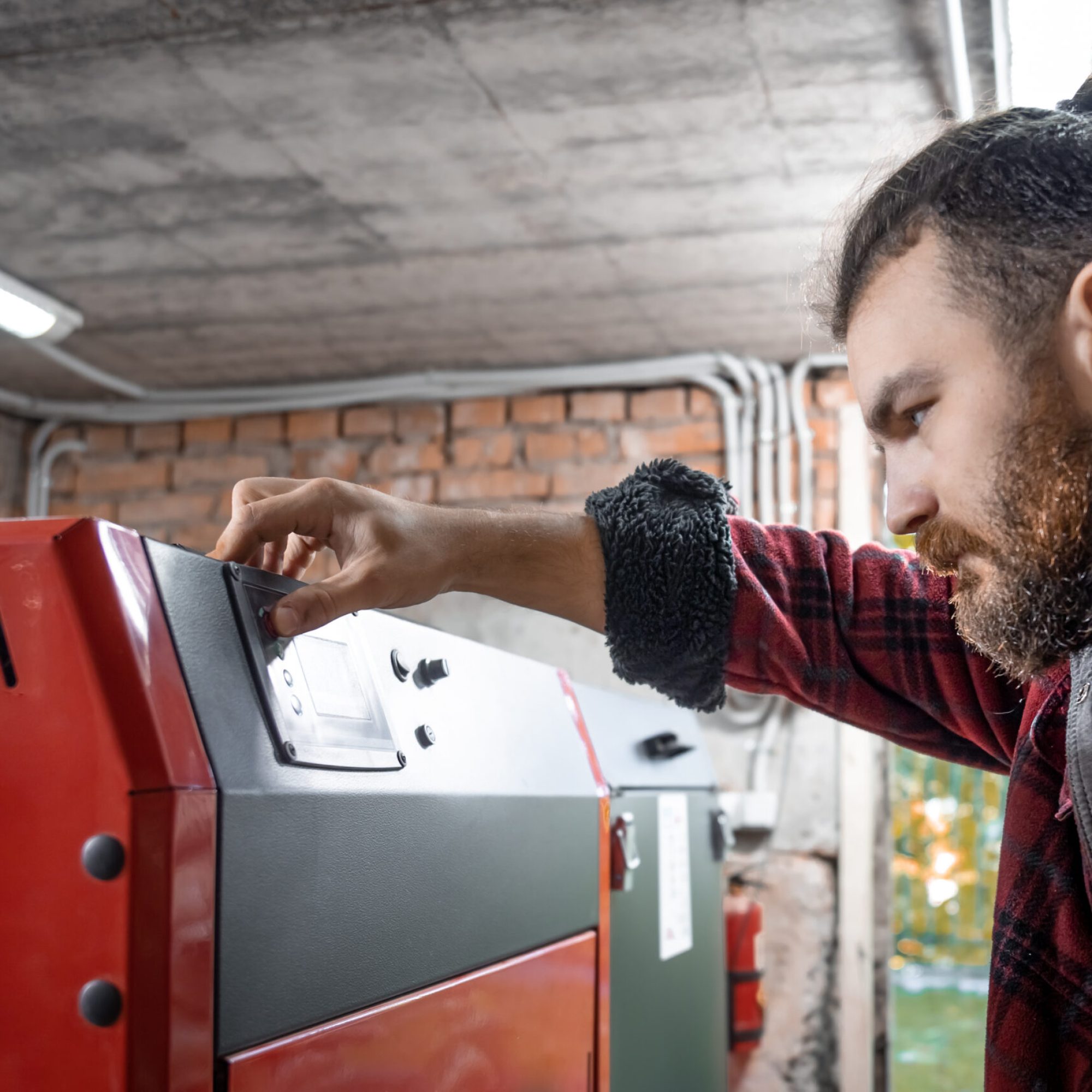 A young man in a room with a solid fuel boiler, working on biofuel, economical heating.